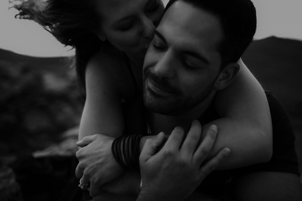Emotional Colorado adventure elopement photographer captures bride kissing groom’s cheek in an intimate black and white mountain portrait Cinematic, windswept, embraced in love adventures in Colorado, Justyna E Butler Photography, Colorado Adventure Wedding Photographer