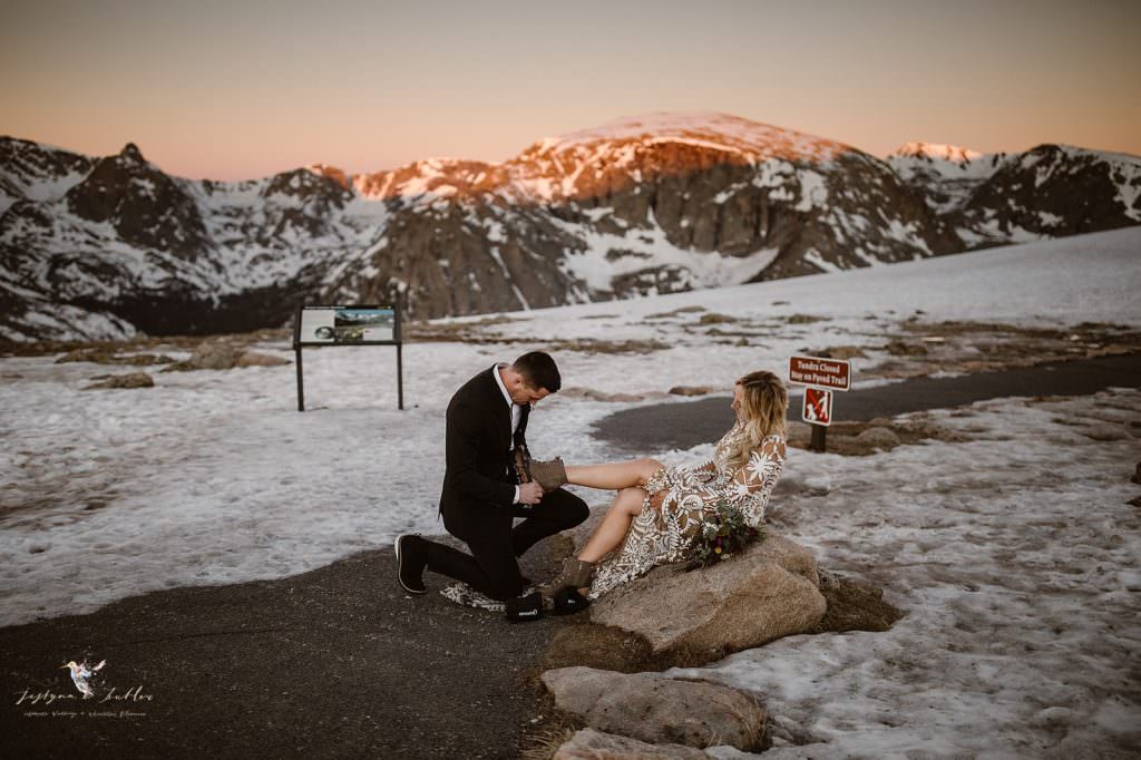 Groom helping his bride put on traction spikes before their snowy Rocky Mountain National Park adventure elopement hike at Rocky Mountain National Park in Estes Park, Colorado 