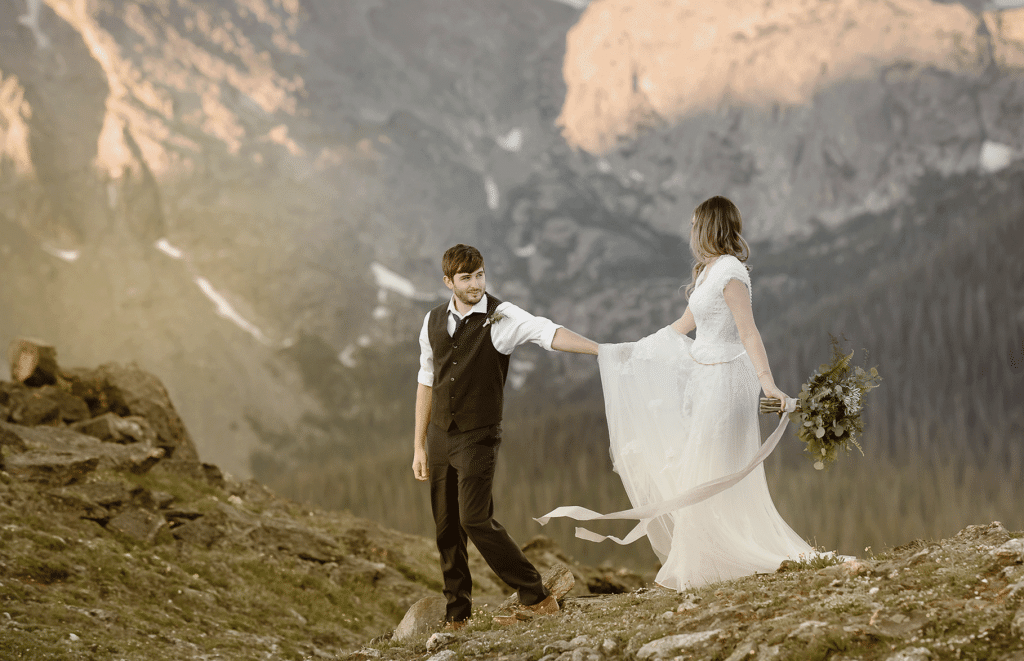 "Romantic mountain elopement in Indian Peaks Wilderness, Colorado – bride in a flowy white dress strolling among alpine glow mountain peaks at sunrise embracing windy Colorado elements captured by Colorado elopement photographer."