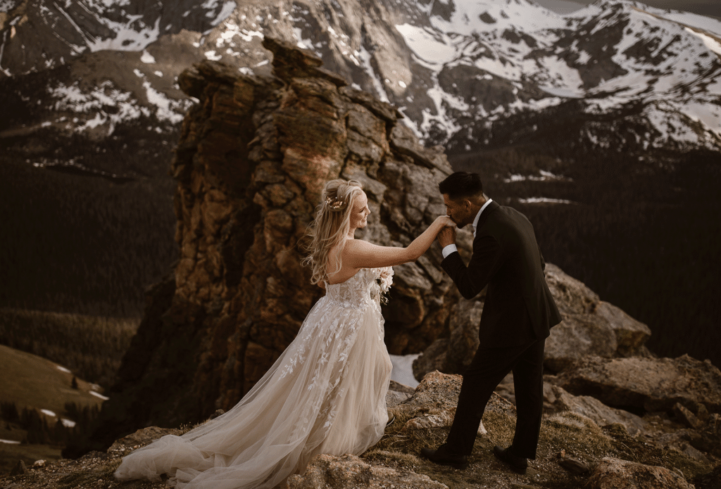 "Elegant Colorado elopement in Rocky Mountain National Park featuring groom kissing bride’s hand against dramatic alpine peaks — photographed by Justyna E Butler, adventurous Colorado Elopement Photographer"
