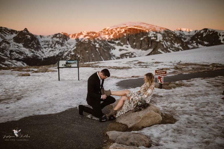 “Adventurous Colorado elopement photography featuring a groom kneeling before his bride at Rocky Mountain National Park with snowy peaks at sunset.”