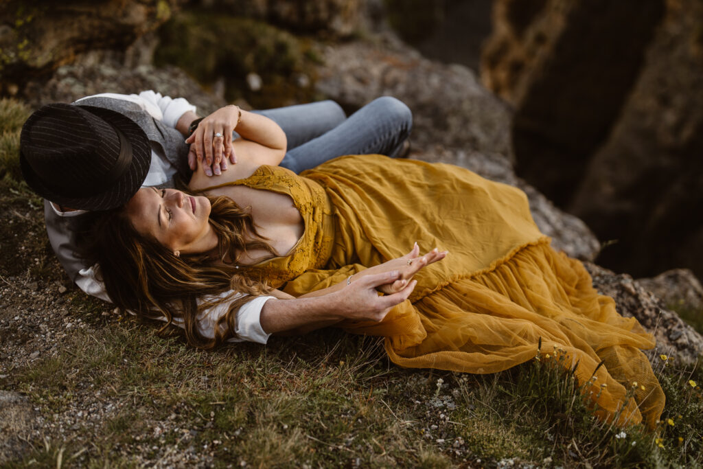 Couple cuddling on a rocky mountainside, woman in mustard yellow dress resting in partner’s arms, intimate Colorado elopement photography.