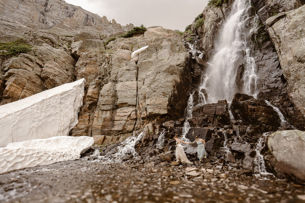 Couple hiking beside Colorado waterfall during adventure elopement at Sky Pond, Rocky Mountain National Park
